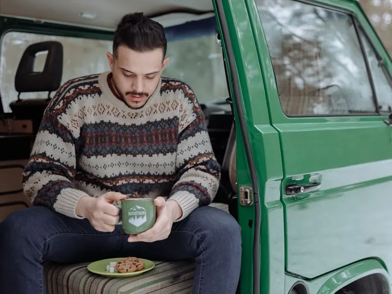 Personne assise à l'arrière d'un van, une tasse de café à la main