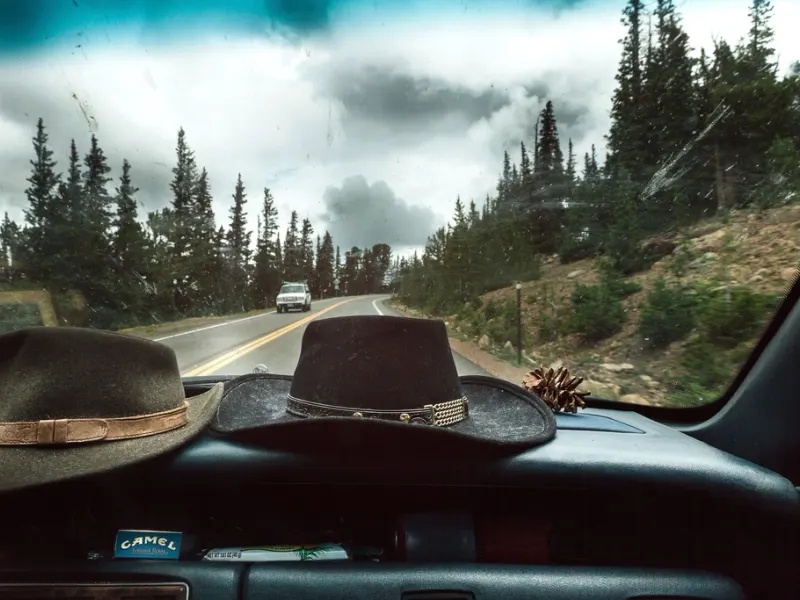 Intérieur d'une voiture sur une route de montagne, deux chapeaux posés sur le tableau de bord