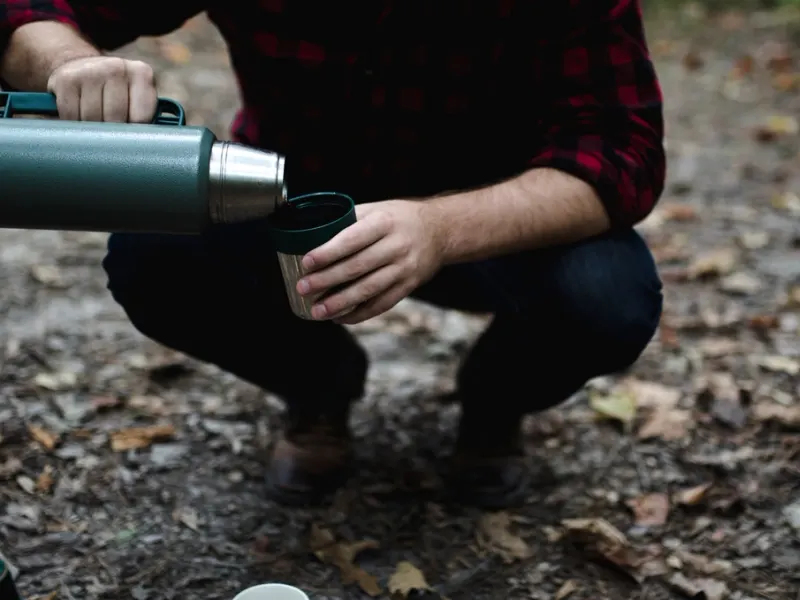 Homme accroupi versant de l'eau chaude d'un thermos dans un gobelet